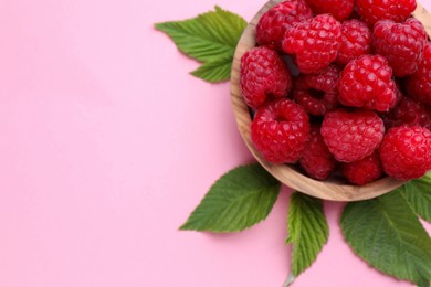 Tasty ripe raspberries and green leaves on pink background, above view. Space for text