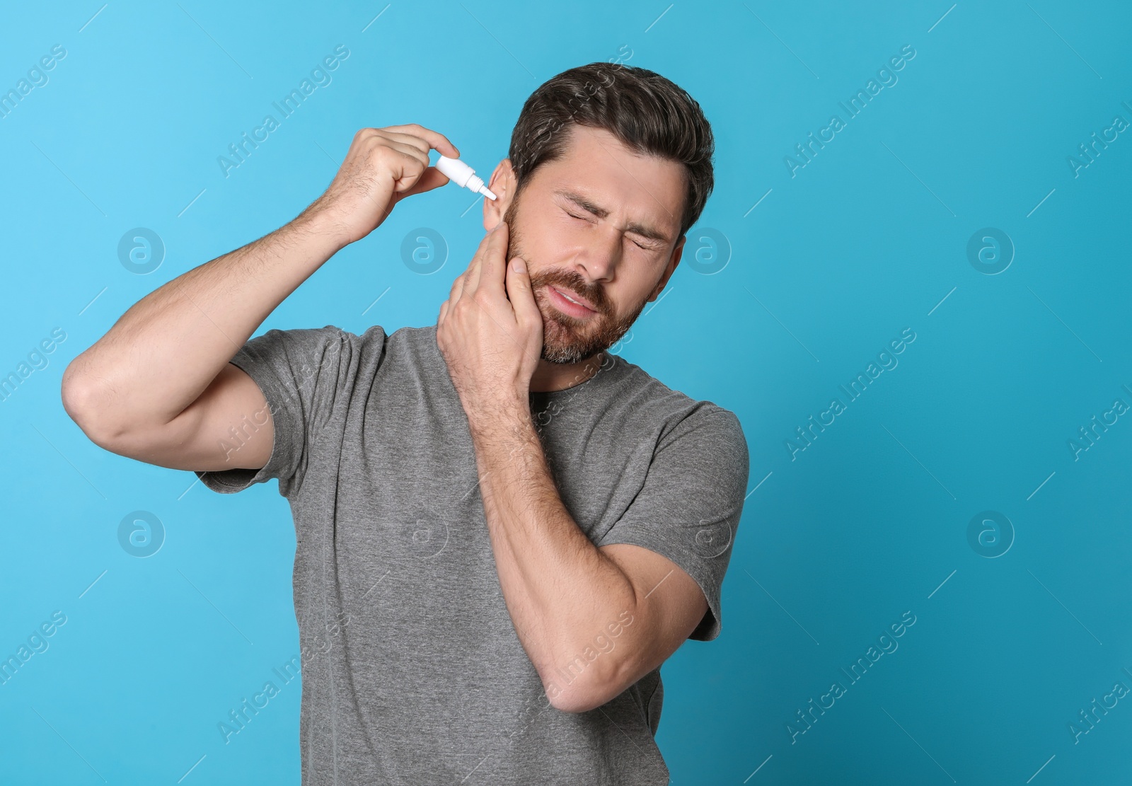 Photo of Man using ear drops on light blue background