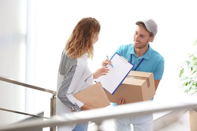 Young woman signing documents after receiving parcels from courier indoors