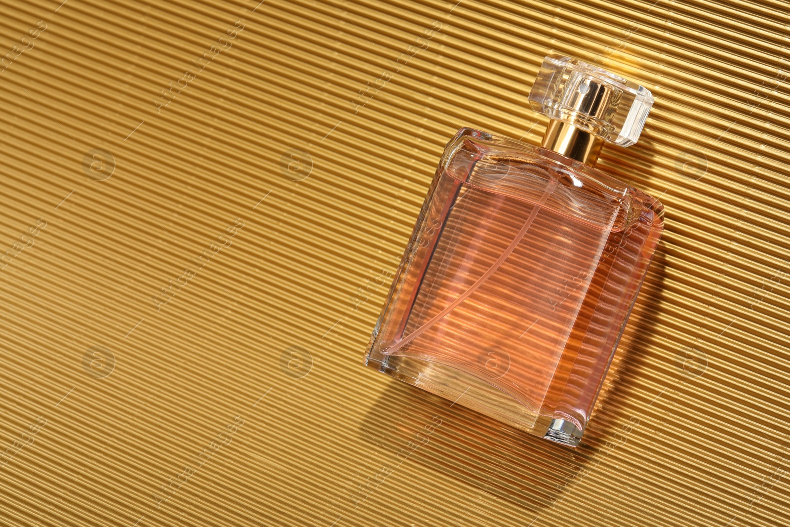 Photo of Luxury women's perfume. Sunlit glass bottle on golden surface, top view. Space for text