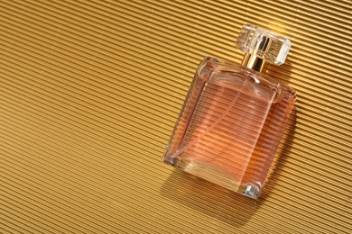 Photo of Luxury women's perfume. Sunlit glass bottle on golden surface, top view. Space for text