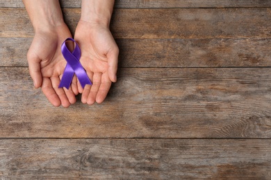 Man with purple awareness ribbon on wooden background, top view with space for text