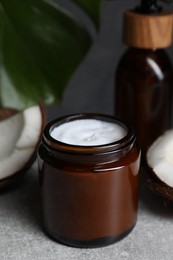 Jar of hand cream and coconut pieces on grey table, closeup