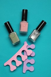 Photo of Nail polishes and separators on turquoise background, flat lay