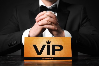 Photo of Man sitting at table with VIP sign on black background, closeup