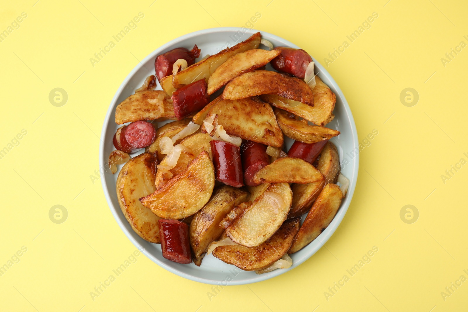 Photo of Delicious baked potato with thin dry smoked sausages and onion on yellow table, top view