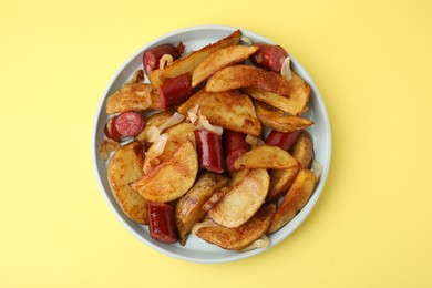 Delicious baked potato with thin dry smoked sausages and onion on yellow table, top view