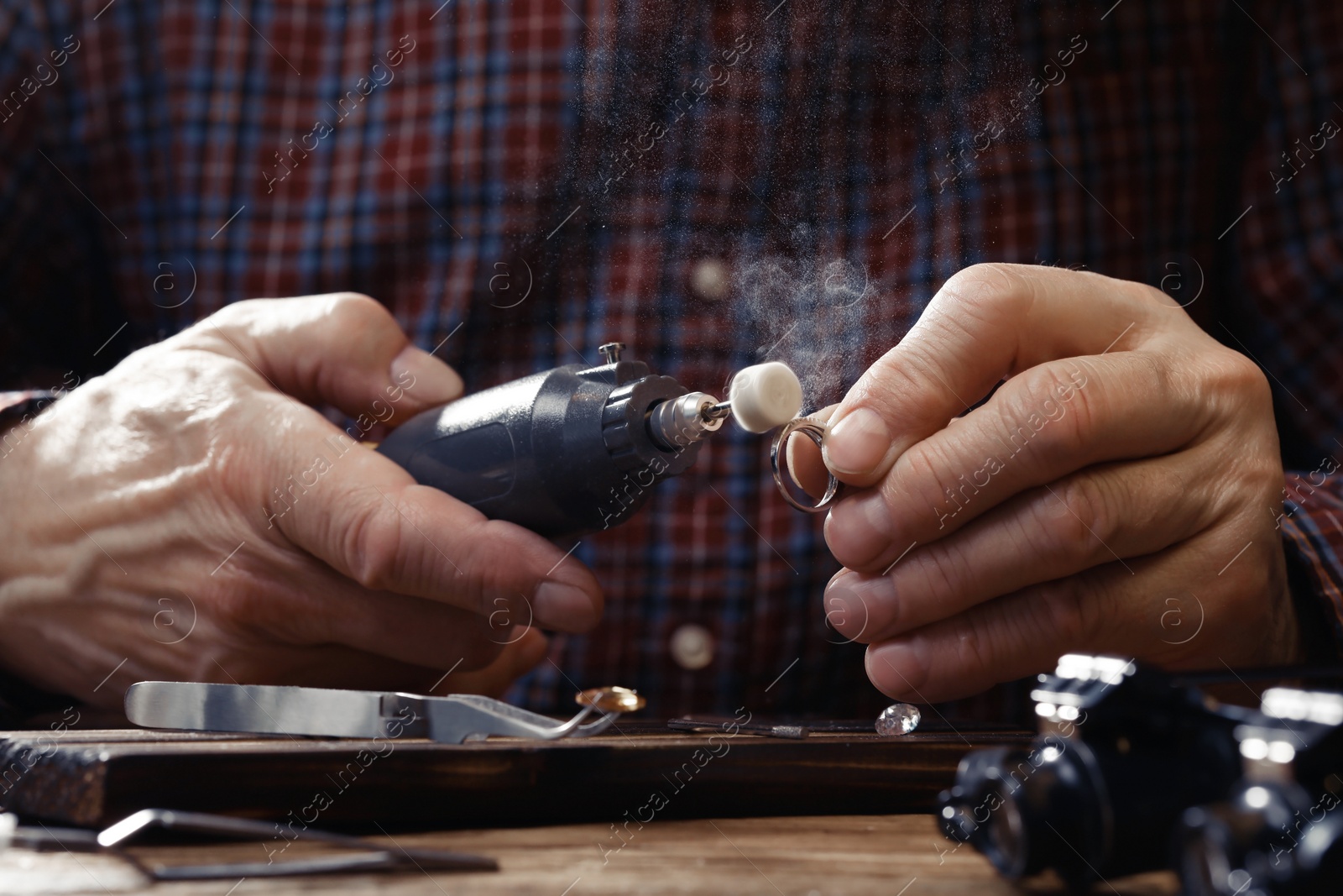 Photo of Professional jeweler working with ring at wooden table, closeup