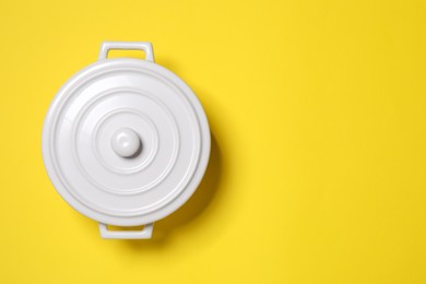 White pot with lid on yellow background, top view. Space for text