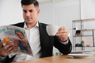 Photo of Man with cup reading magazine at table in office