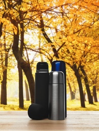 Image of Different thermoses on wooden table in autumn park