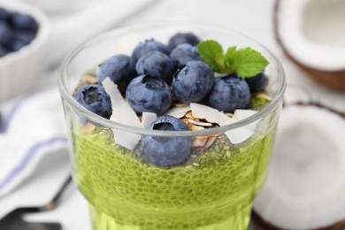 Photo of Tasty matcha chia pudding with coconut and blueberries in glass, closeup. Healthy breakfast