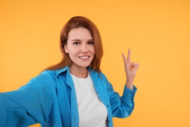 Beautiful woman taking selfie on orange background