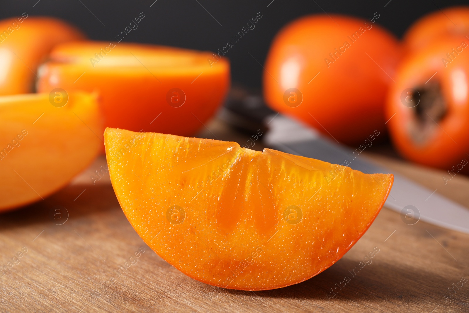 Photo of Piece of delicious ripe persimmon on wooden board, closeup