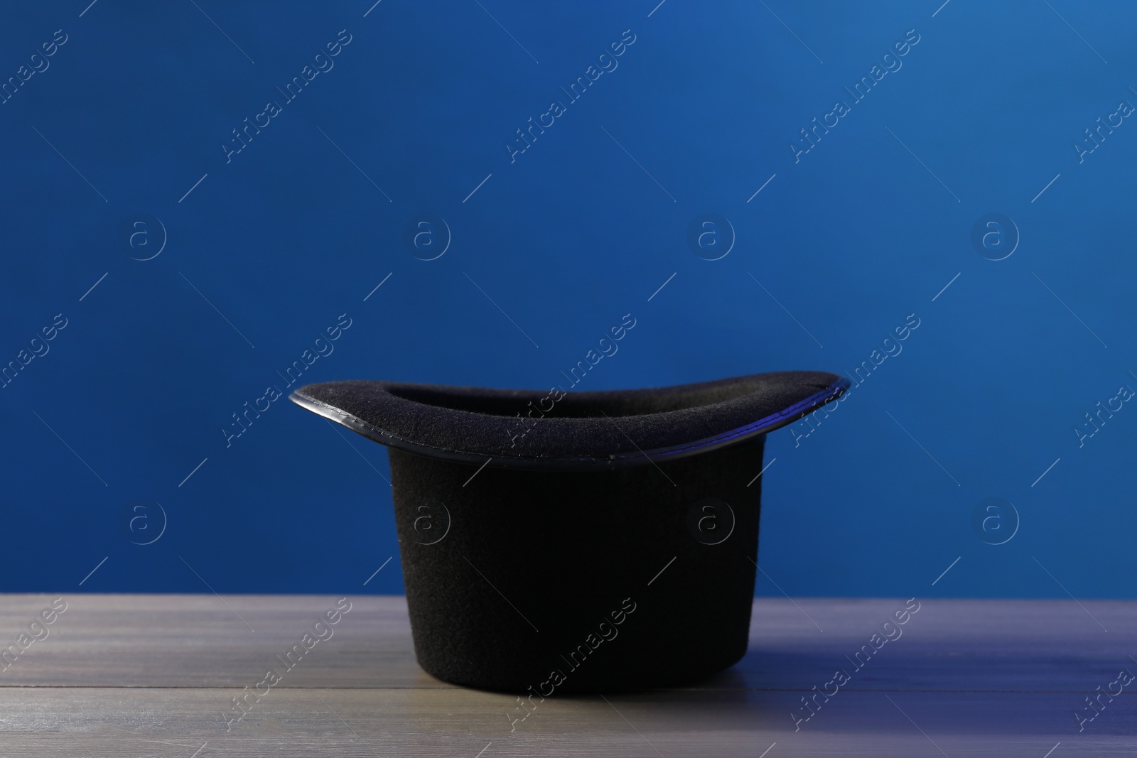 Photo of Magician's hat on wooden table against blue background