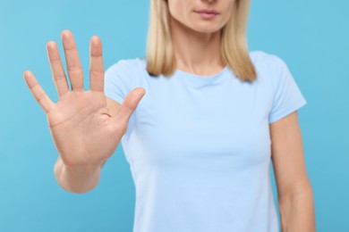 Woman showing stop gesture on light blue background, closeup