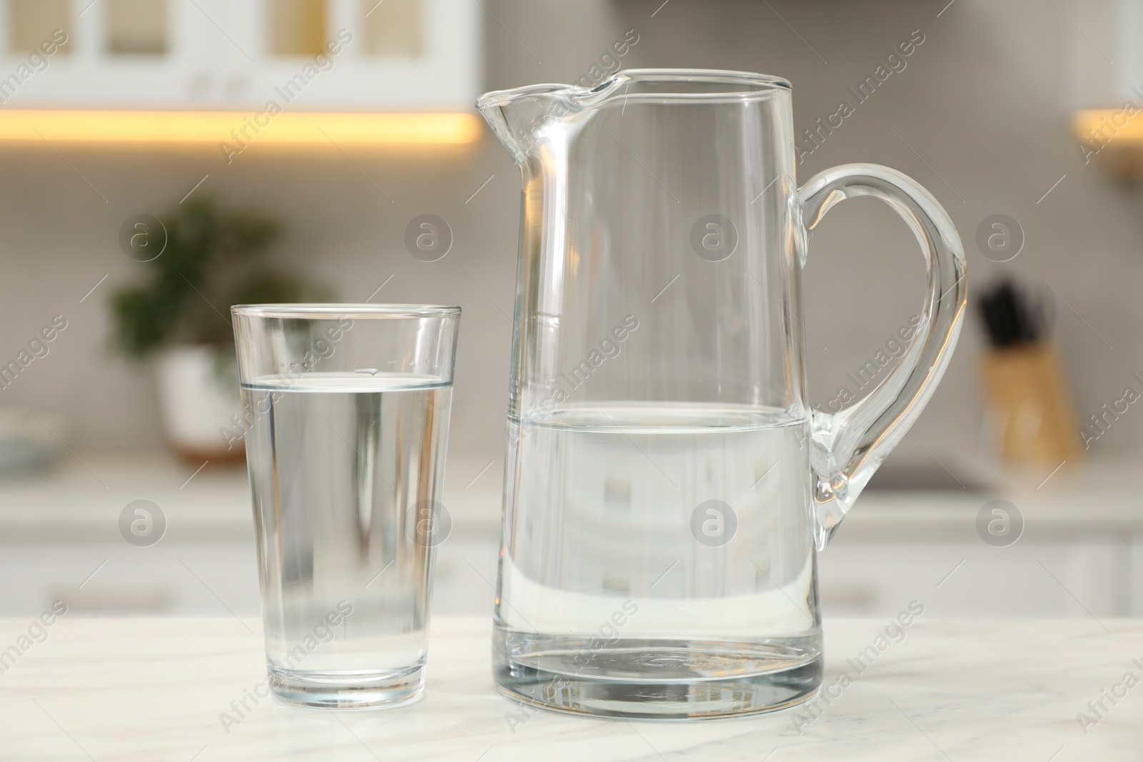 Photo of Jug and glass with clear water on white table in kitchen, closeup