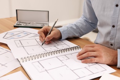 Photo of Man drawing in sketchbook with pencil at wooden table, closeup