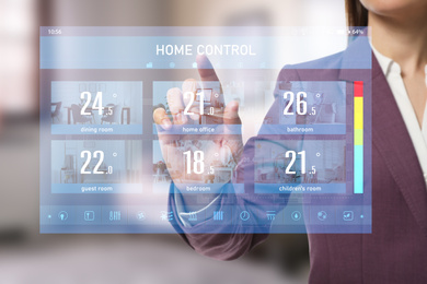 Image of Woman using touchscreen panel to set indoor temperature, closeup. Smart home automation system