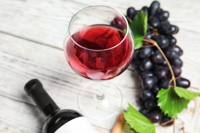 Glass and bottle of red wine with fresh ripe juicy grapes on table