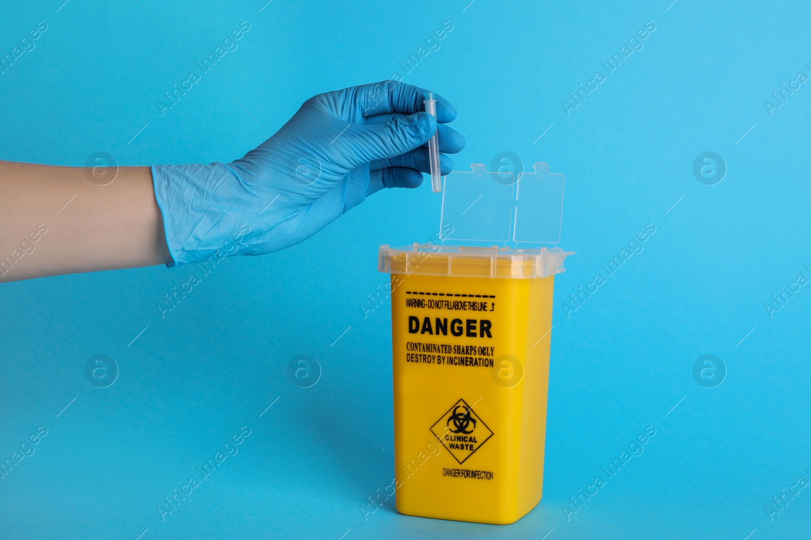 Photo of Doctor throwing used syringe needle into sharps container on light blue background, closeup