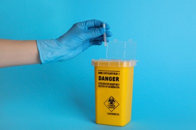 Photo of Doctor throwing used syringe needle into sharps container on light blue background, closeup