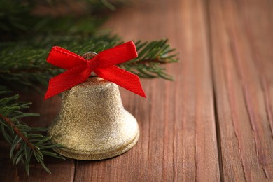Photo of Bell with red bow and fir branches on wooden table, closeup with space for text. Christmas decor