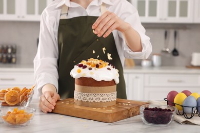 Photo of Woman decorating delicious Easter cake with almond flakes at white marble table in kitchen, closeup