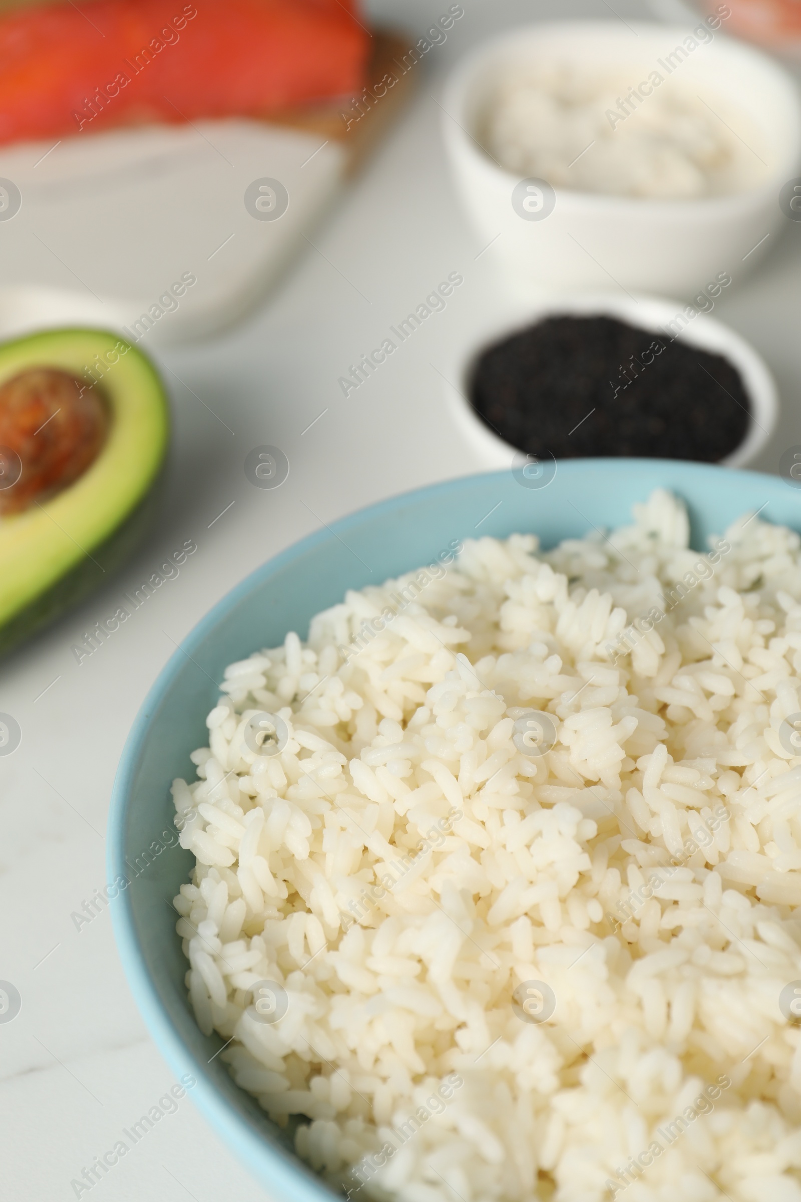 Photo of Cooked rice in bowl and other ingredients for sushi on white table, closeup