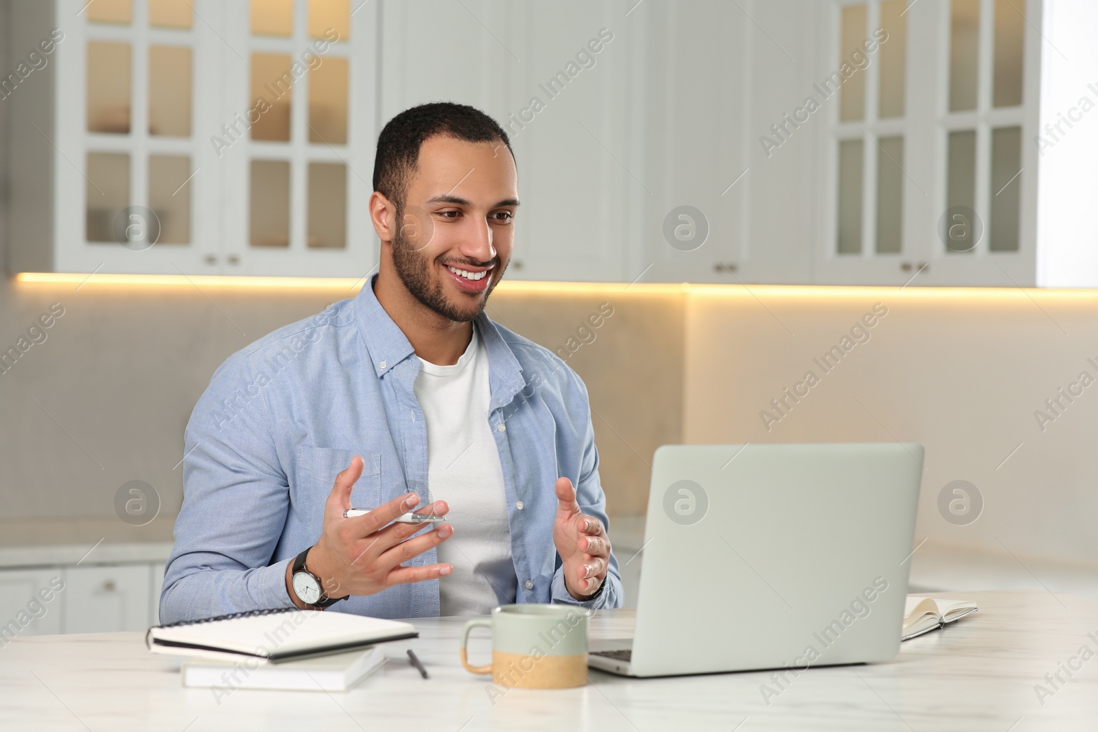 Photo of Young man having online video chat at desk in kitchen. Home office