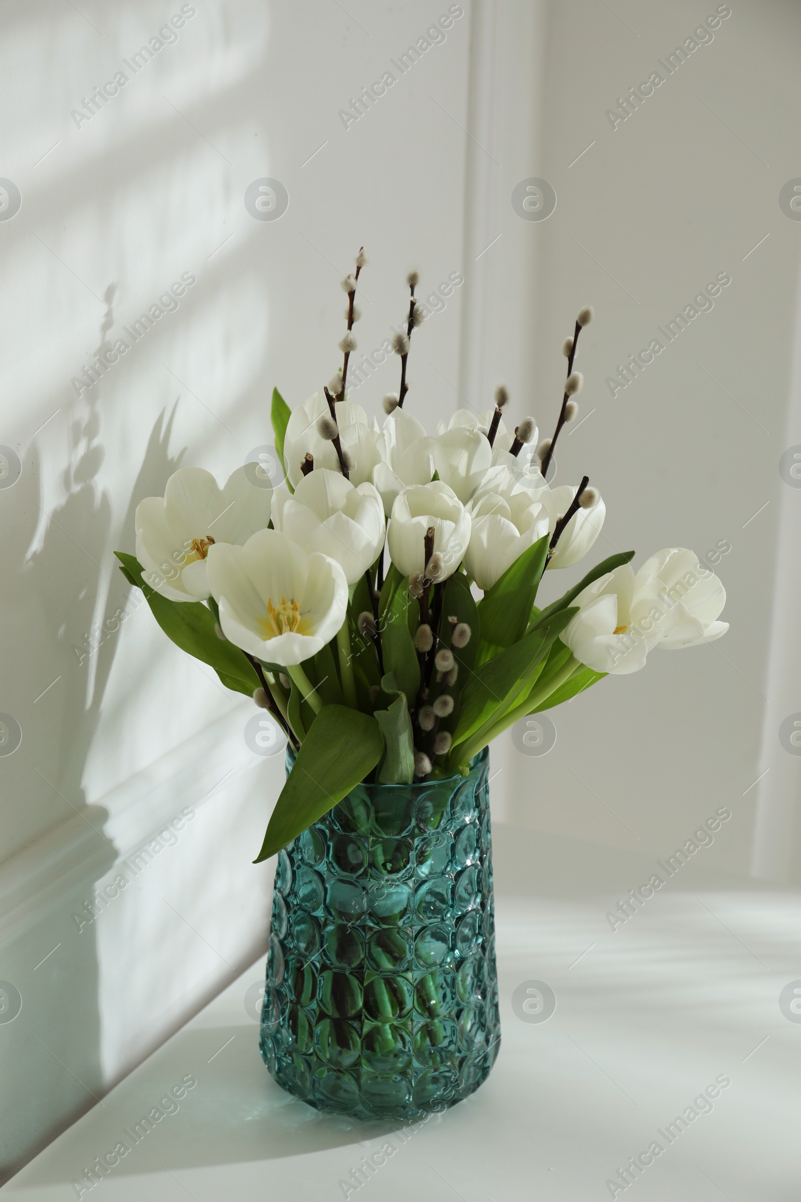 Photo of Beautiful bouquet of willow branches and tulips in vase near white wall