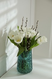 Photo of Beautiful bouquet of willow branches and tulips in vase near white wall