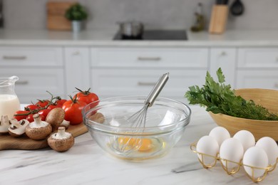 Whisk, bowl, and different ingredients on white marble table indoors