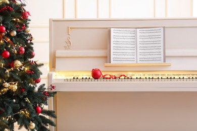 White piano with festive decor and music sheets near Christmas tree indoors