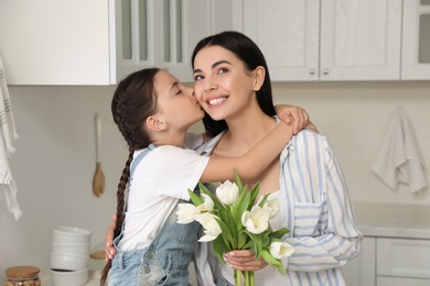 Photo of Little daughter congratulating her mom in kitchen at home. Happy Mother's Day