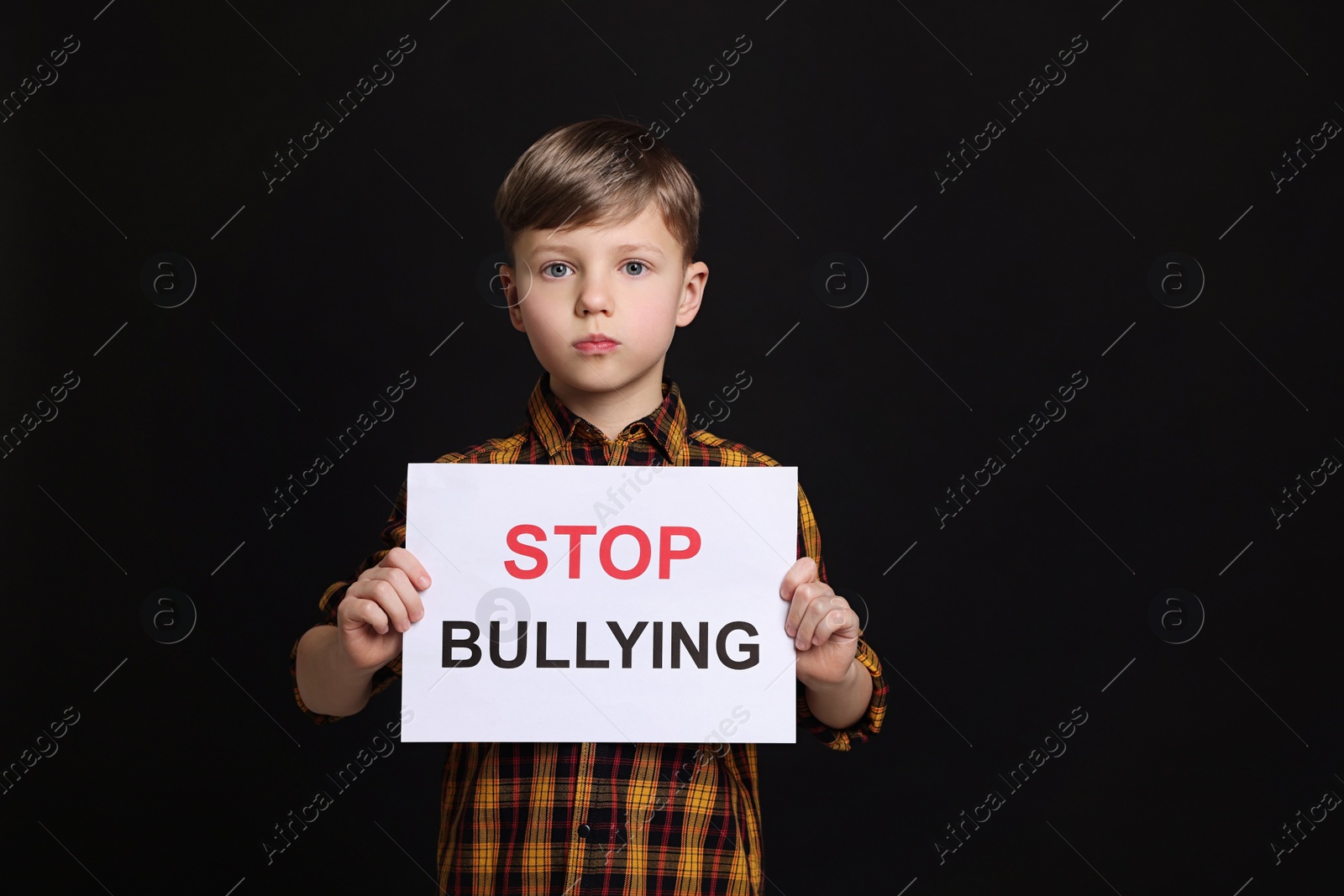 Photo of Boy holding sign with phrase Stop Bullying on black background