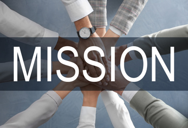People holding hands together over grey background and text MISSION, top view