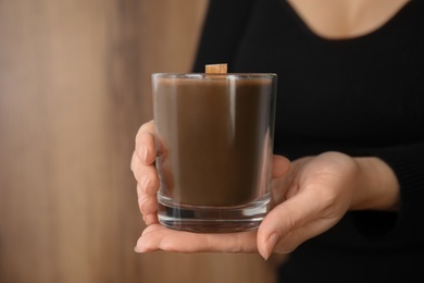 Photo of Woman holding candle with wooden wick on brown background, closeup