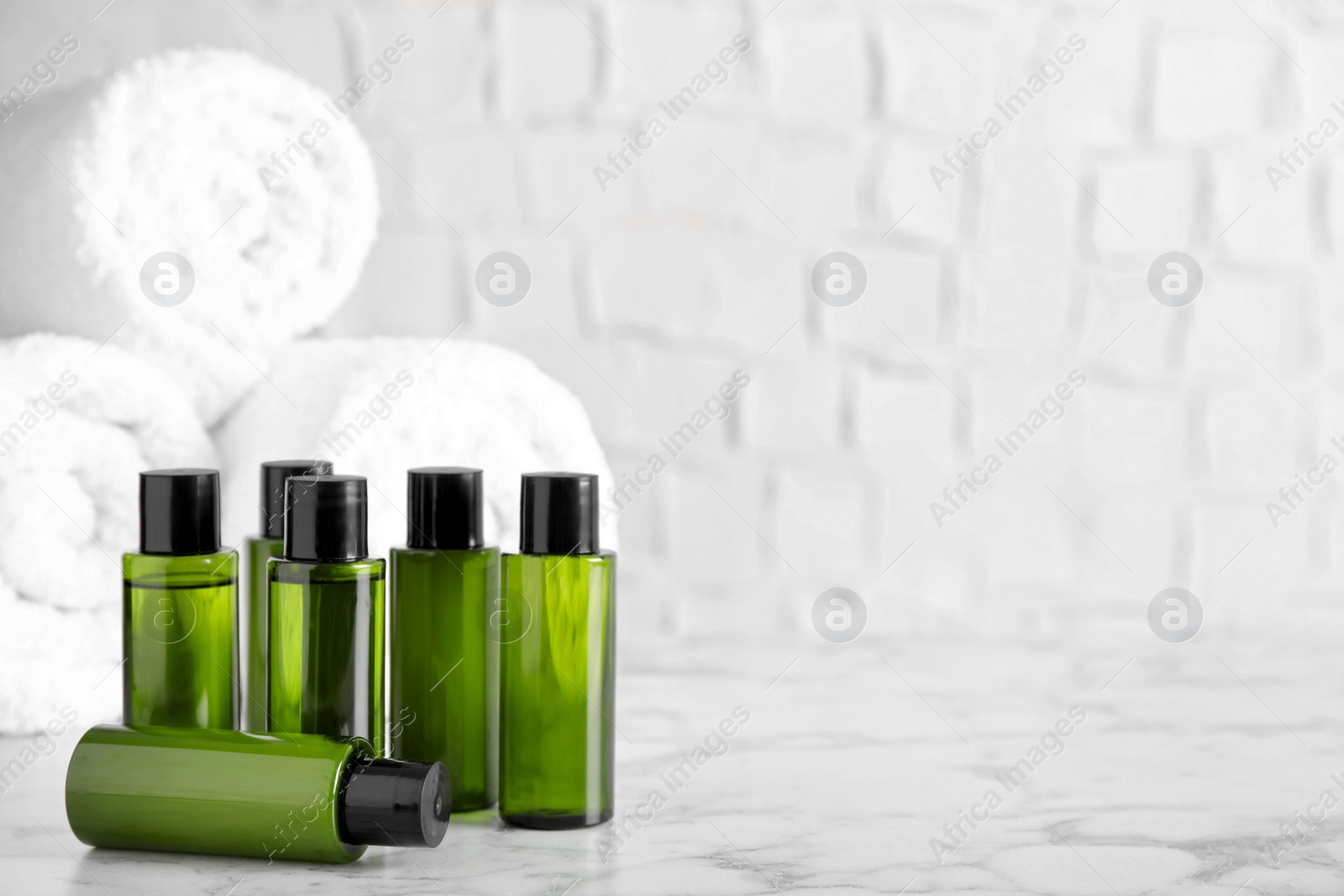 Photo of Mini bottles with cosmetic products and towels on marble table against white background. Space for text