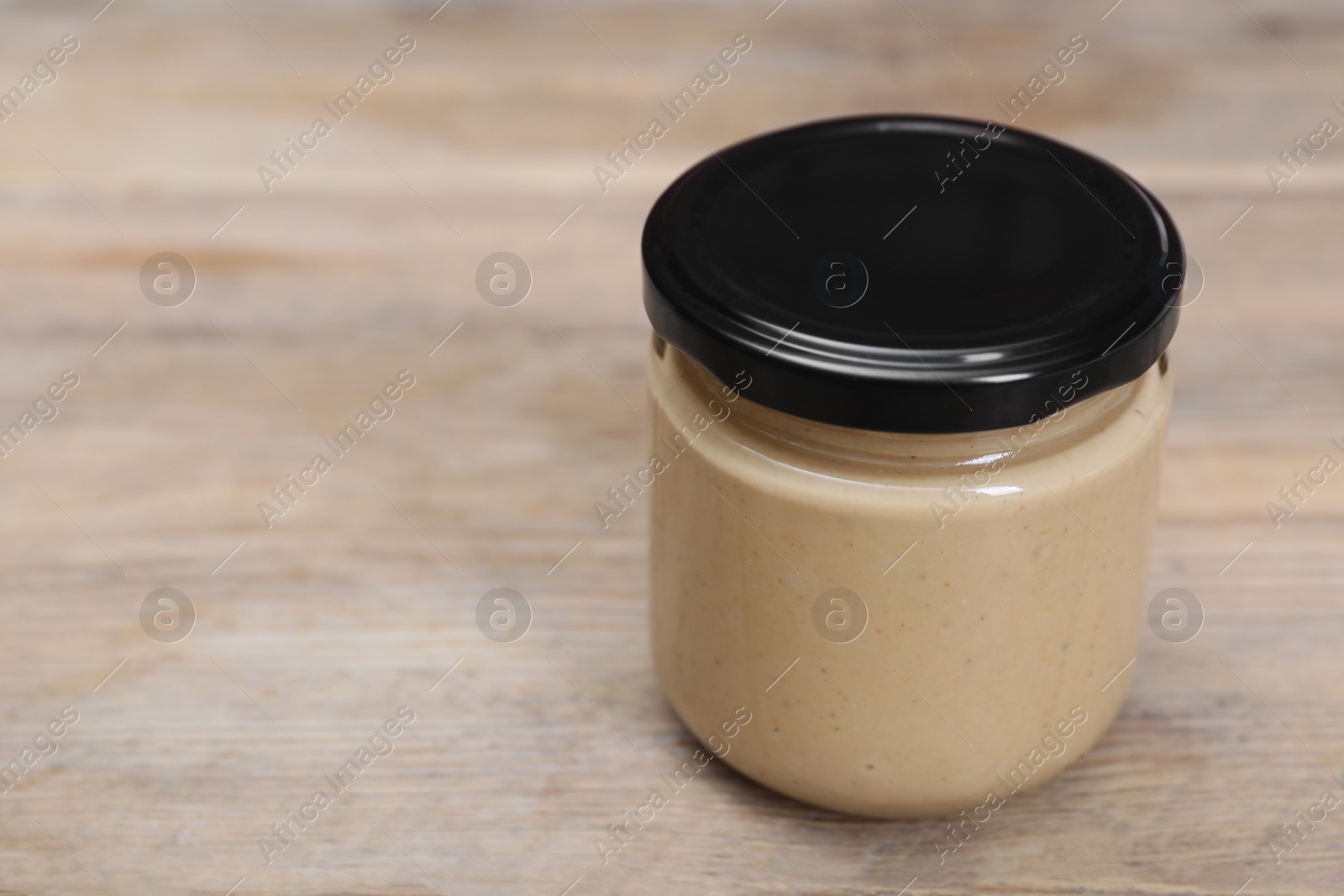 Photo of Tasty nut paste in jar on wooden table, closeup. Space for text