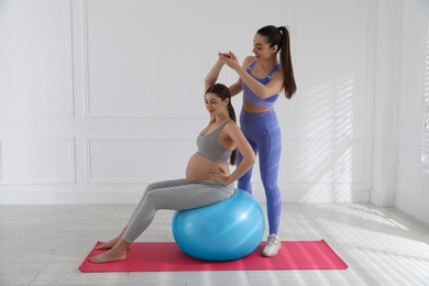 Trainer working with pregnant woman in gym. Preparation for child birth