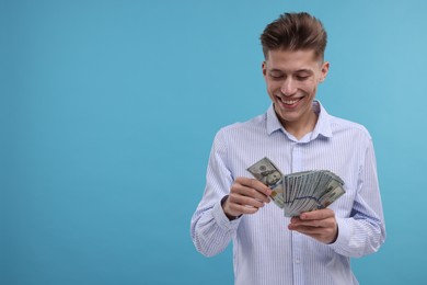 Happy man counting dollar banknotes on light blue background. Space for text