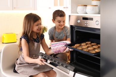 Cute little children taking cookies out of oven in kitchen. Cooking pastry