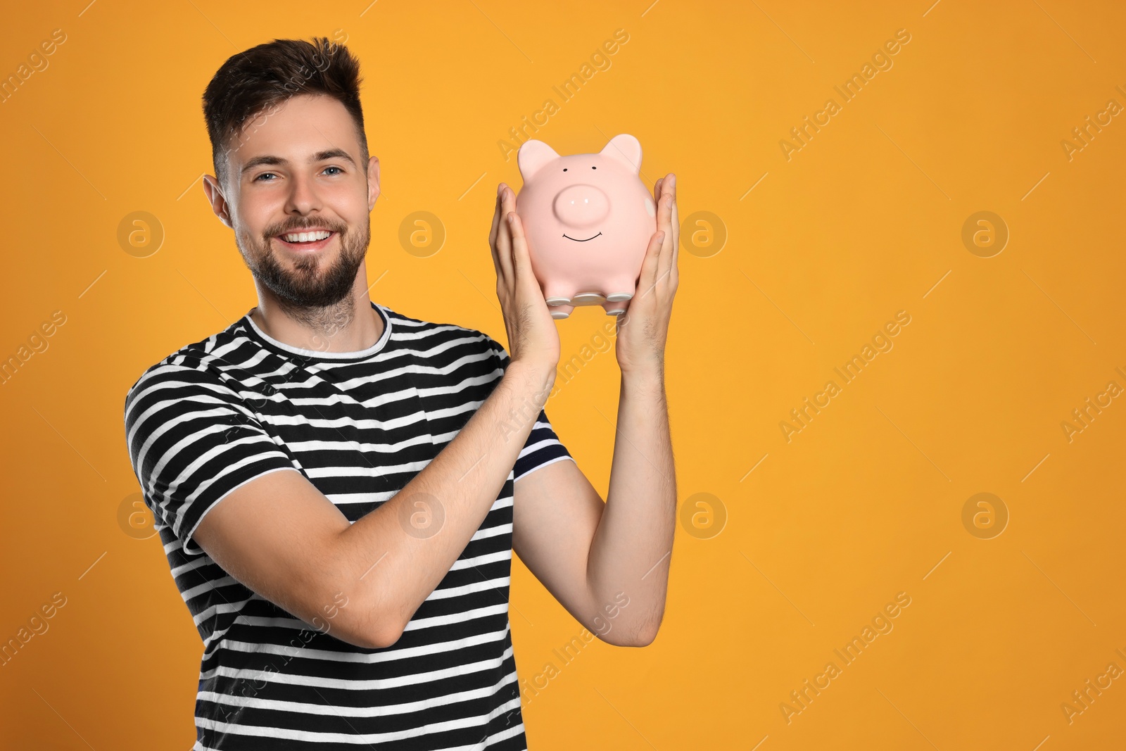 Photo of Happy young man with piggy bank on orange background. Space for text