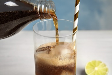 Photo of Pouring refreshing soda drink into glass with ice cubes and straw on table, closeup