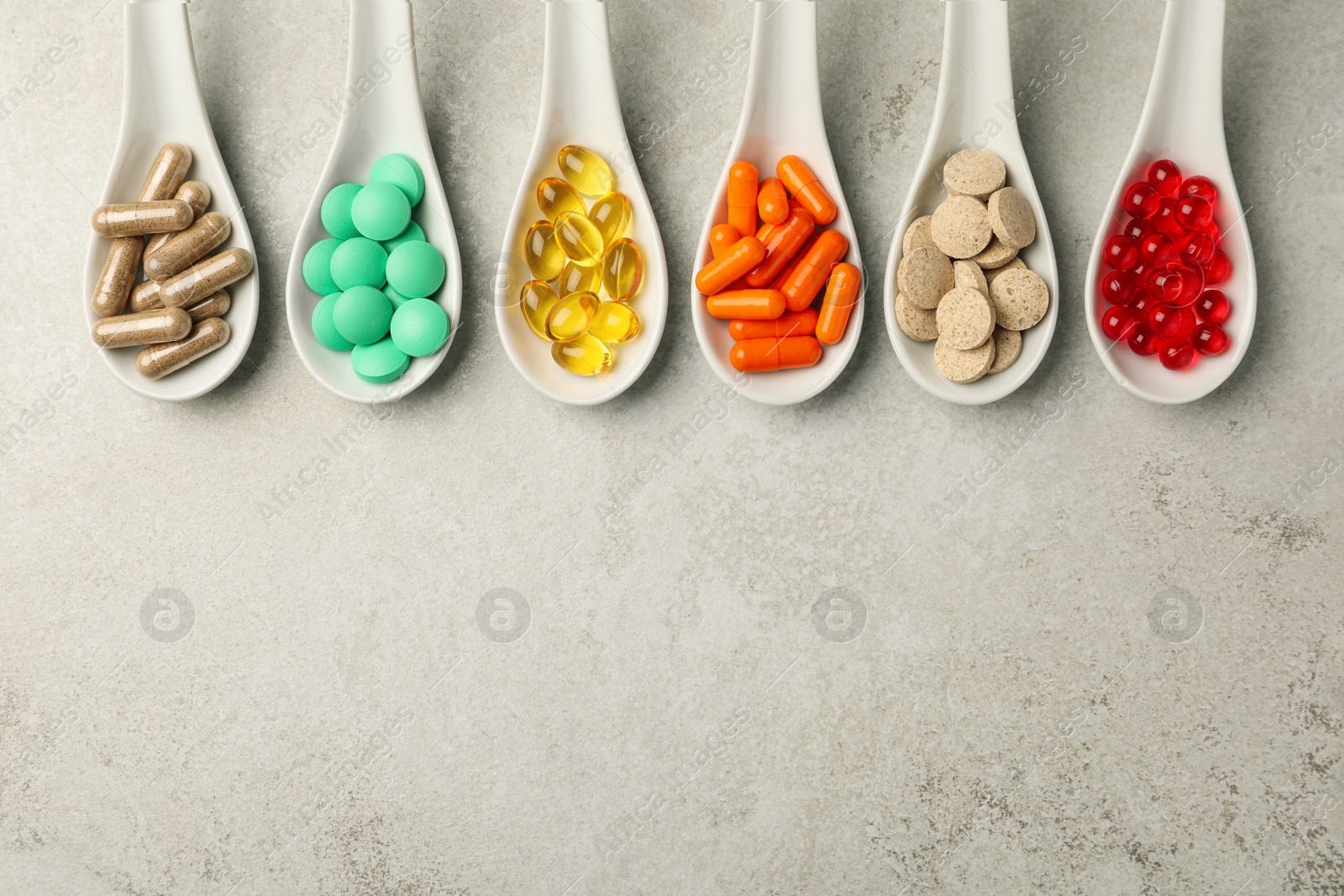 Photo of Spoons with different dietary supplements on light grey table, flat lay. Space for text