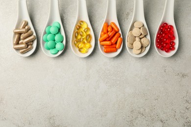 Spoons with different dietary supplements on light grey table, flat lay. Space for text