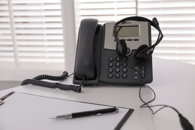 Photo of Desktop telephone with headset on white table in office. Hotline service