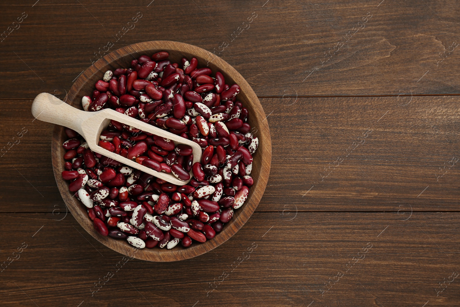 Photo of Bowl with dry kidney beans and scoop on wooden table, top view. Space for text