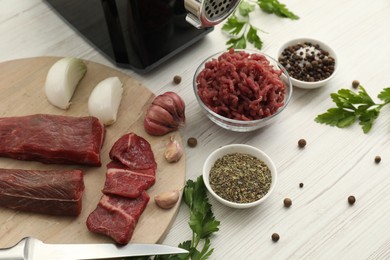 Meat grinder, beef, onion, garlic, parsley and spices on white wooden table